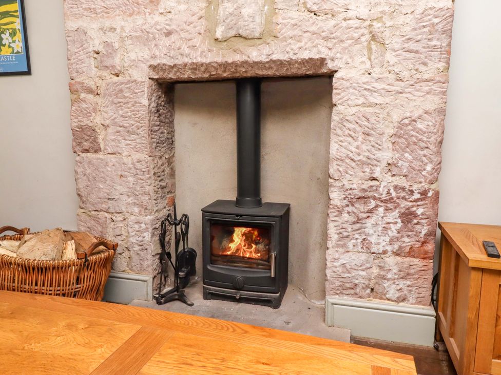 A fireplace with a wood stove and a basket of firewood at Gamekeepers Cottage in Chillingham near Chatton