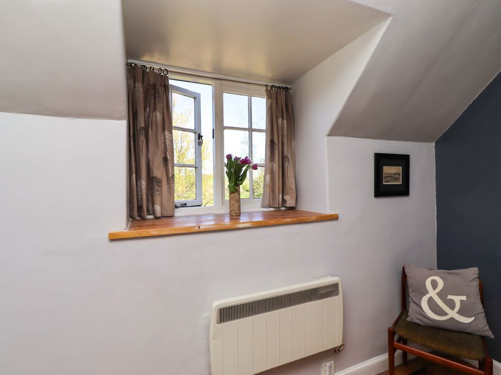An interior with a window, curtain, flowers in a vase, radiator, and chair at Gamekeepers Cottage, Chillingham near Chatton