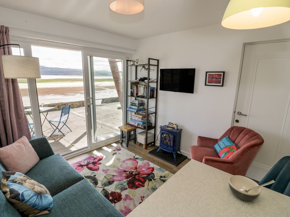 A living room with a sofa and books on a shelf at Lan y Mor in Porthmadog