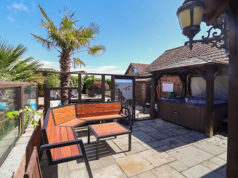 An outdoor seating area with a hot tub and palm trees at The Old Byres in Washford near Watchet