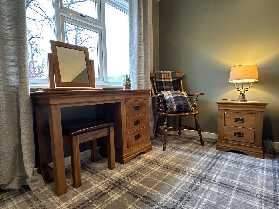A bedroom with wooden furniture including a table, chair, lamp, and nightstand at White Hillocks Cottage Kirriemuir