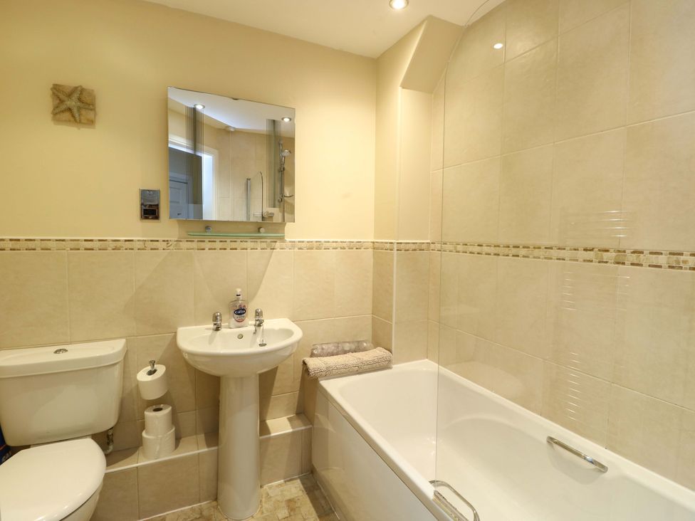 A bathroom with a bathtub, sink, toilet, and mirror at Y Enciliad in Rhosneigr