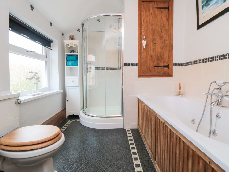 A bathroom with a shower, bathtub, and storage shelf at Sands End Cottage in Marske-by-the-Sea