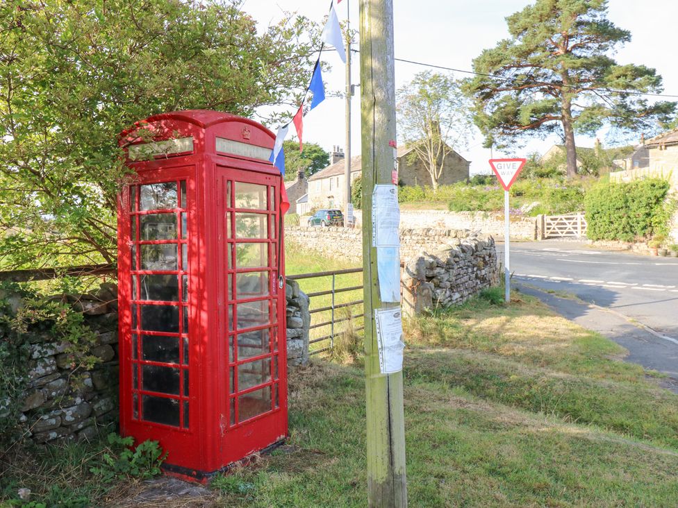A red telephone box near a road sign and gate in Romaldkirk near Middleton-in-Teesdale