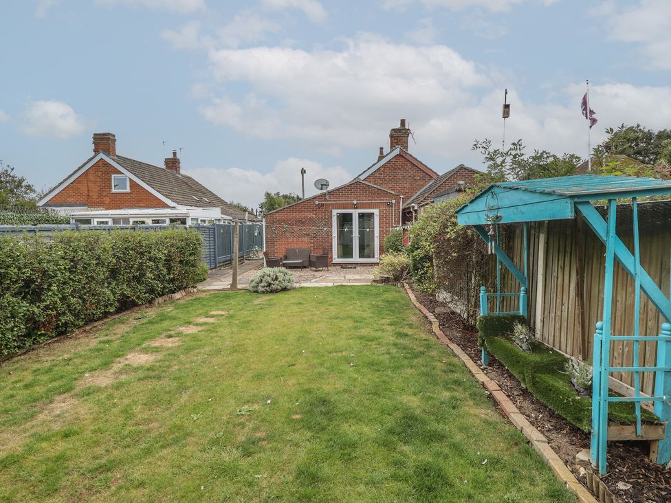 A garden with grass and a patio area at Herby's Retreat in Sutton-On-Sea