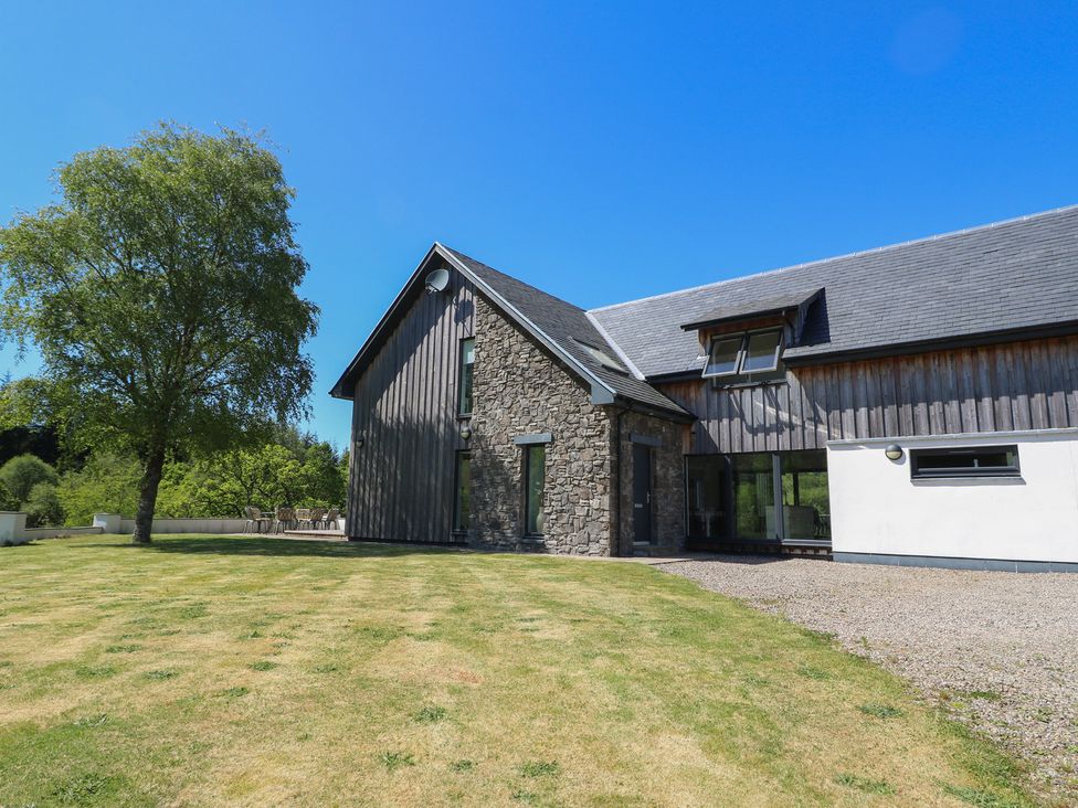 A modern house with stone and wood exterior next to a tree and lawn at Sobrachan in Kilmartin