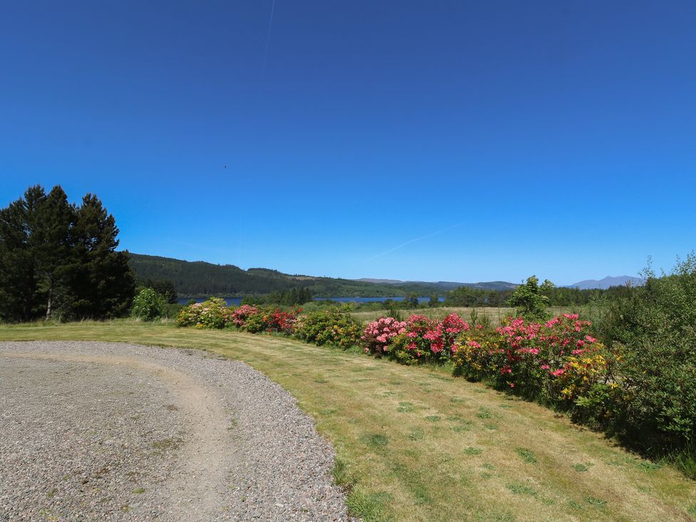 A garden with a gravel path and flowering bushes with trees and a lake in the background at Sobrachan in Kilmartin