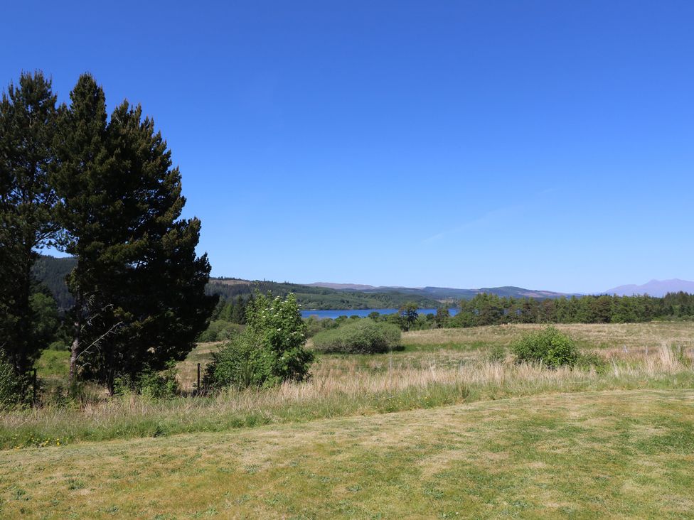 A grassy field with trees and a lake in the distance under a clear blue sky at Sobrachan in Kilmartin