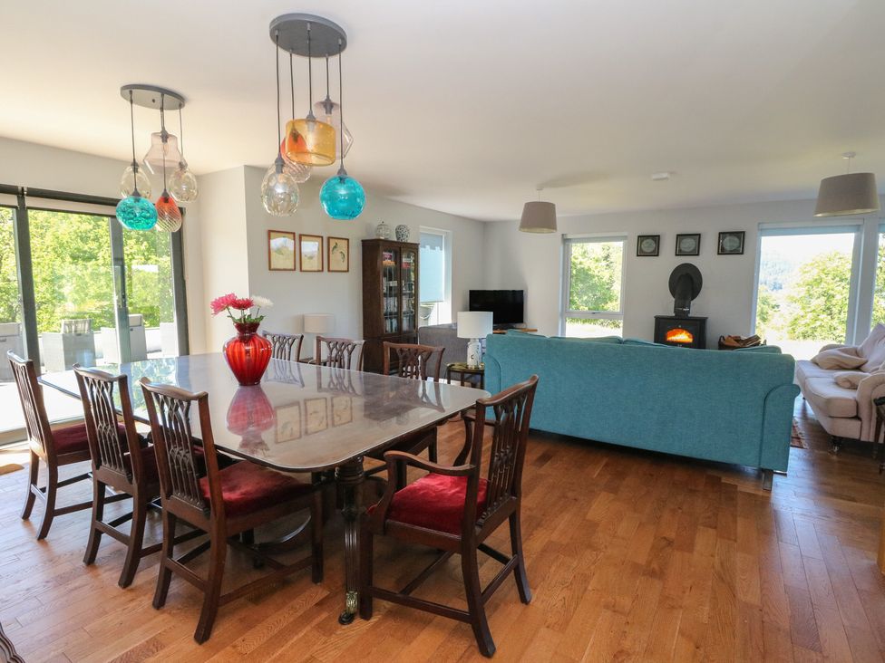 A dining area with a large glass table and wooden chairs next to a living space with blue and beige sofas and a wood stove at Sobrachan in Kilmartin
