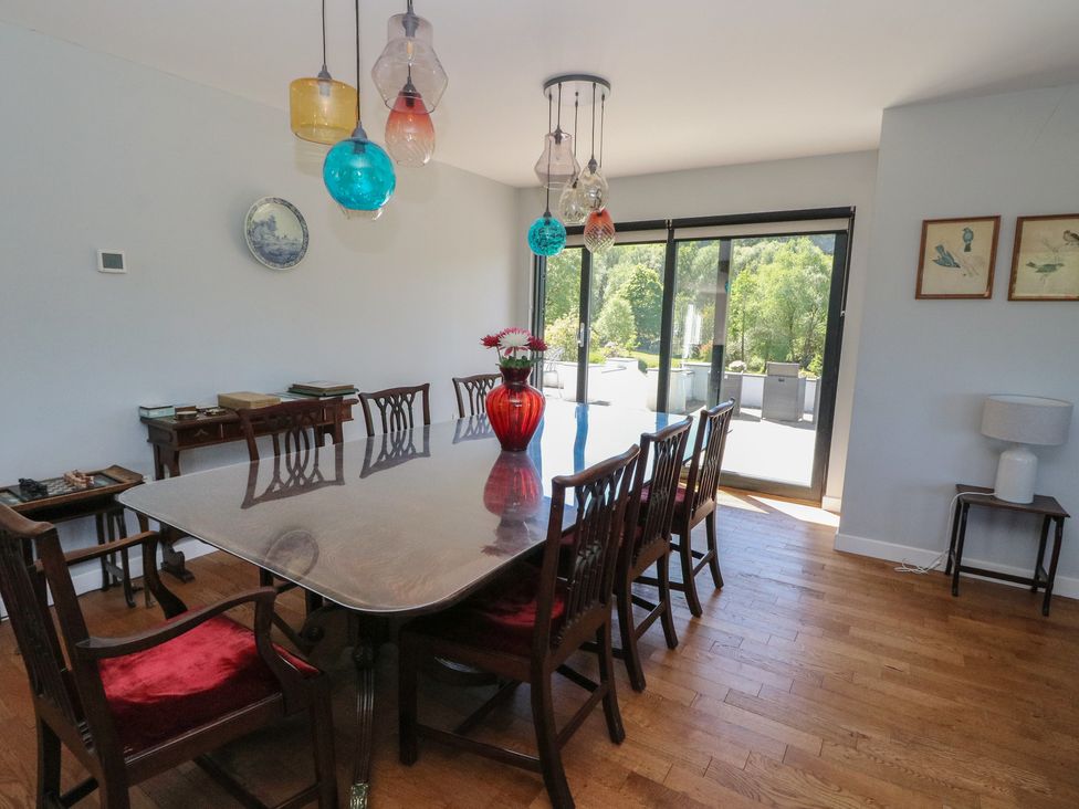 A dining room with a large table and chairs a red vase with flowers and glass pendant lights at Sobrachan in Kilmartin