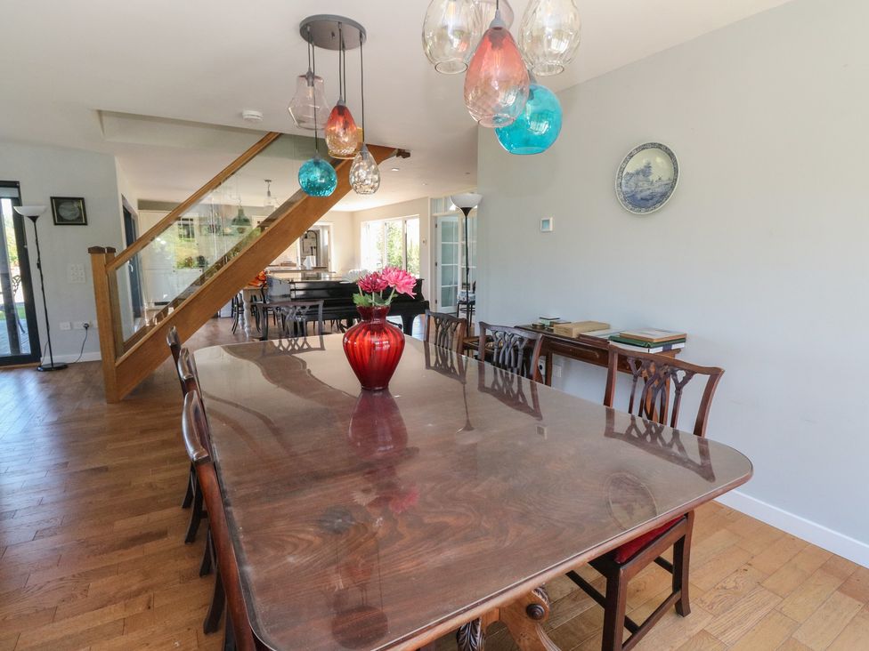 A dining room with a wooden table and chairs a red vase with flowers and colorful hanging lights at Sobrachan in Kilmartin