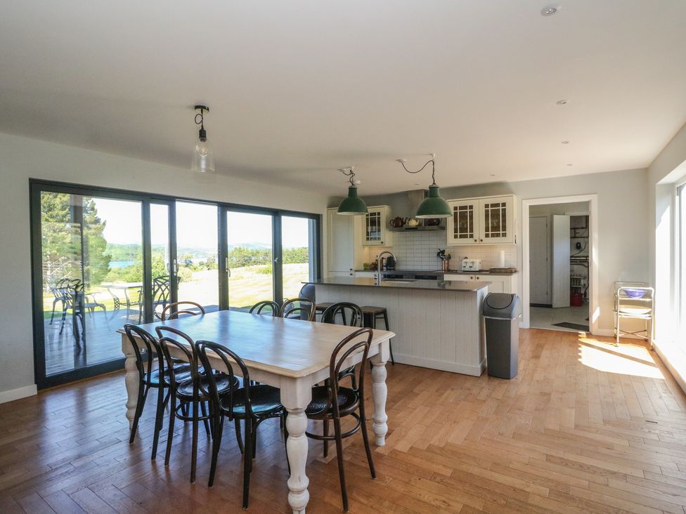 A kitchen and dining area with a wooden table and black chairs next to large glass doors and a kitchen island with green pendant lights at Sobrachan in Kilmartin