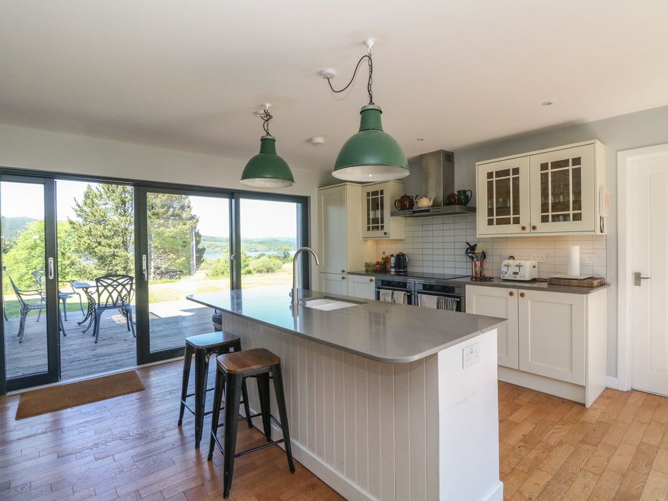 A kitchen with island counter and stools next to sliding glass doors leading to an outdoor patio at Sobrachan in Kilmartin