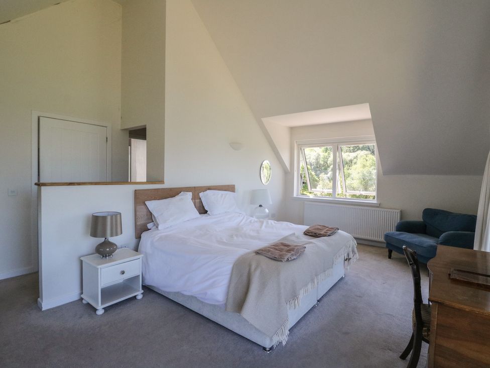 A bedroom with a double bed bedside tables a blue sofa a wooden desk and a window at Sobrachan in Kilmartin