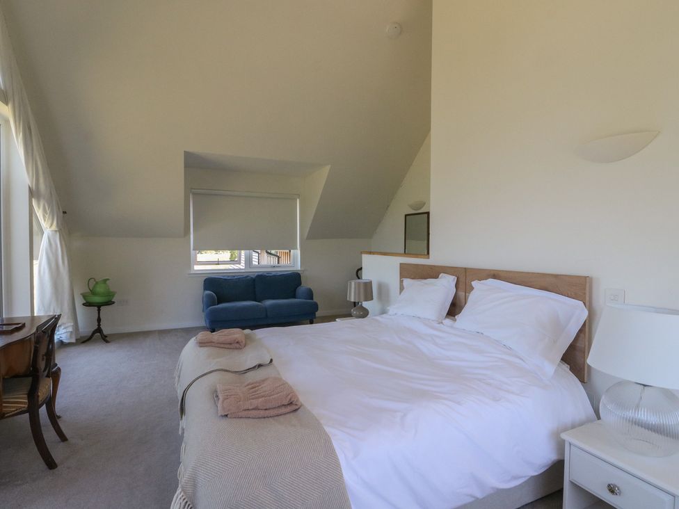 A bedroom with a double bed a blue sofa a wooden desk and a window with closed blinds at Sobrachan in Kilmartin