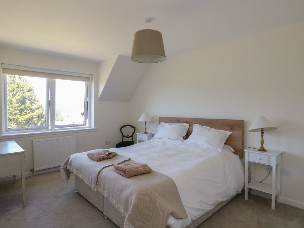 A bedroom with a double bed two bedside tables with lamps a window and a chair at Sobrachan in Kilmartin