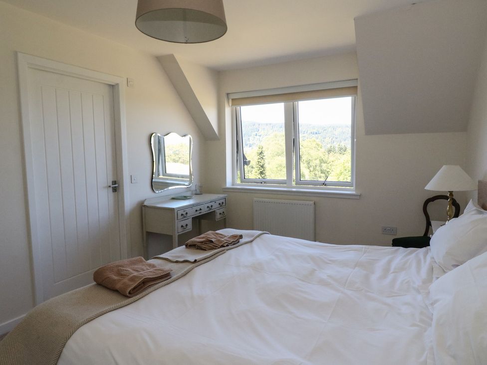 A bedroom with a bed a dressing table a chair and a window showing trees at Sobrachan in Kilmartin