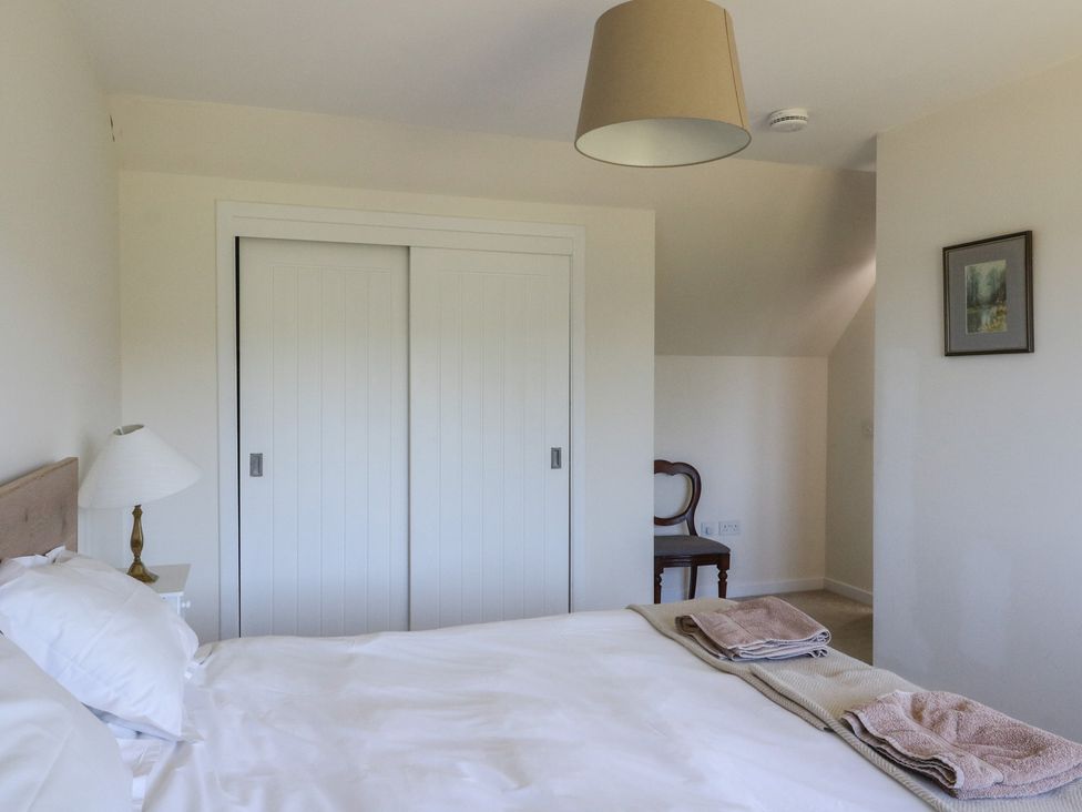 A bedroom with a bed with white bedding and towels on it a bedside table with a lamp a chair in the corner sliding closet doors and a framed picture on the wall at Sobrachan in Kilmartin