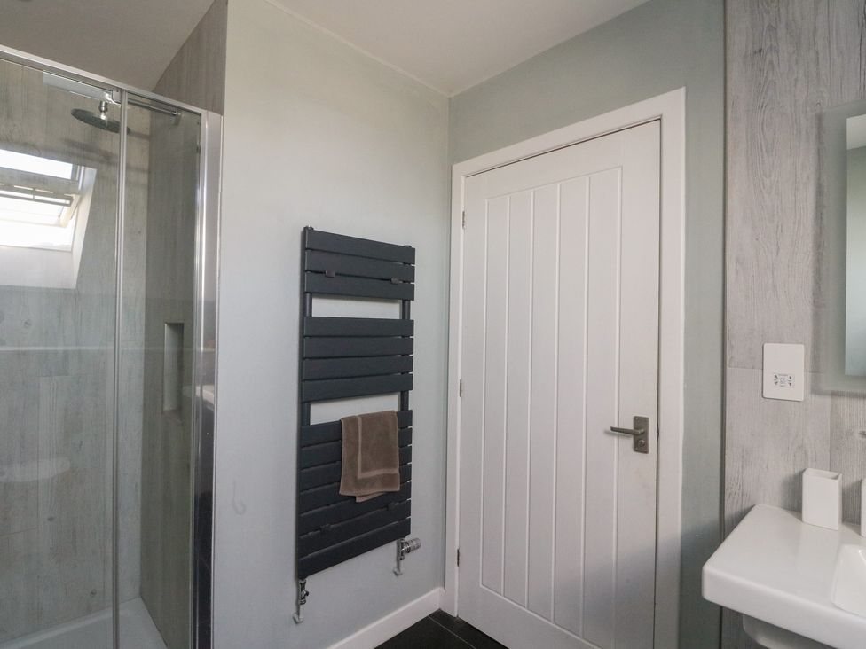 A bathroom with a shower enclosure a black towel radiator a white door and a white sink at Sobrachan in Kilmartin