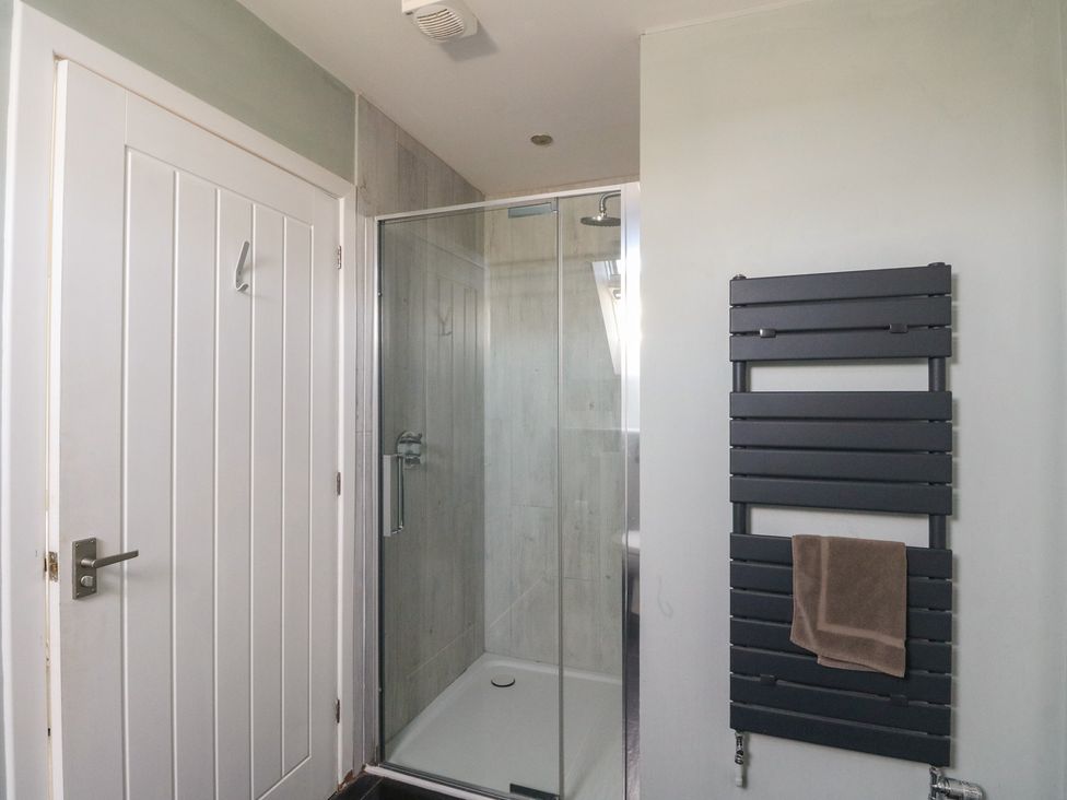 A bathroom with a glass shower enclosure a white door and a black towel radiator with a brown towel at Sobrachan in Kilmartin