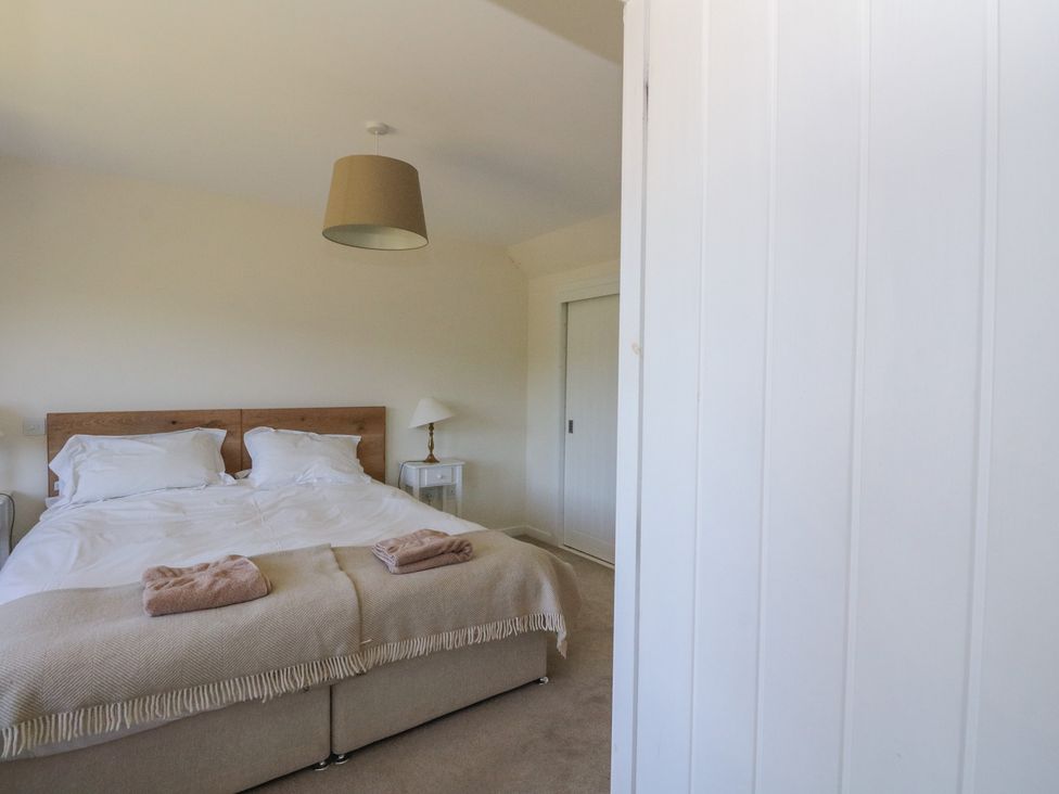 A bedroom with a double bed covered with white bedding and beige blankets with two folded towels on top at Sobrachan in Kilmartin