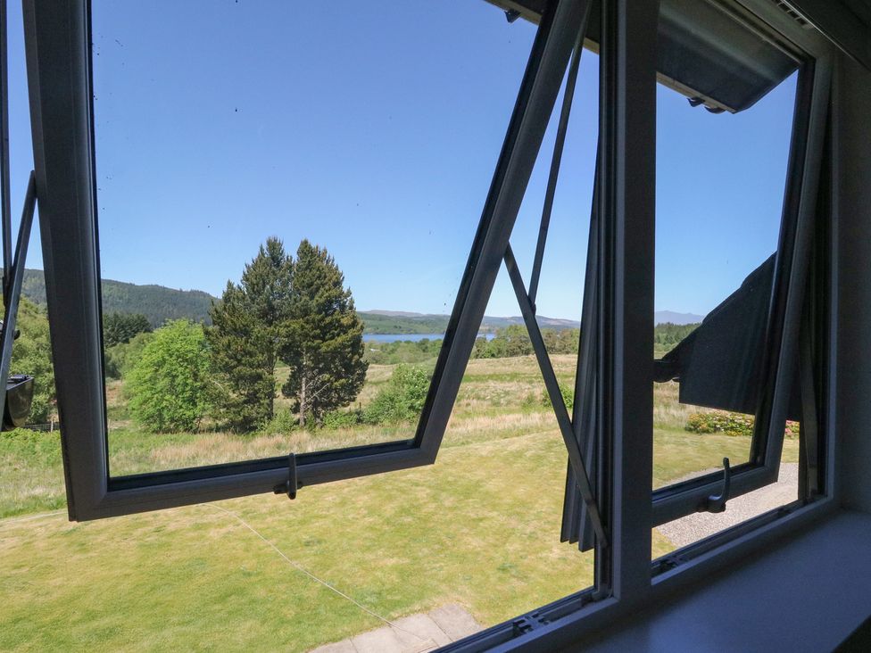A view through open windows showing grass, trees, hills, and a lake at Sobrachan in Kilmartin