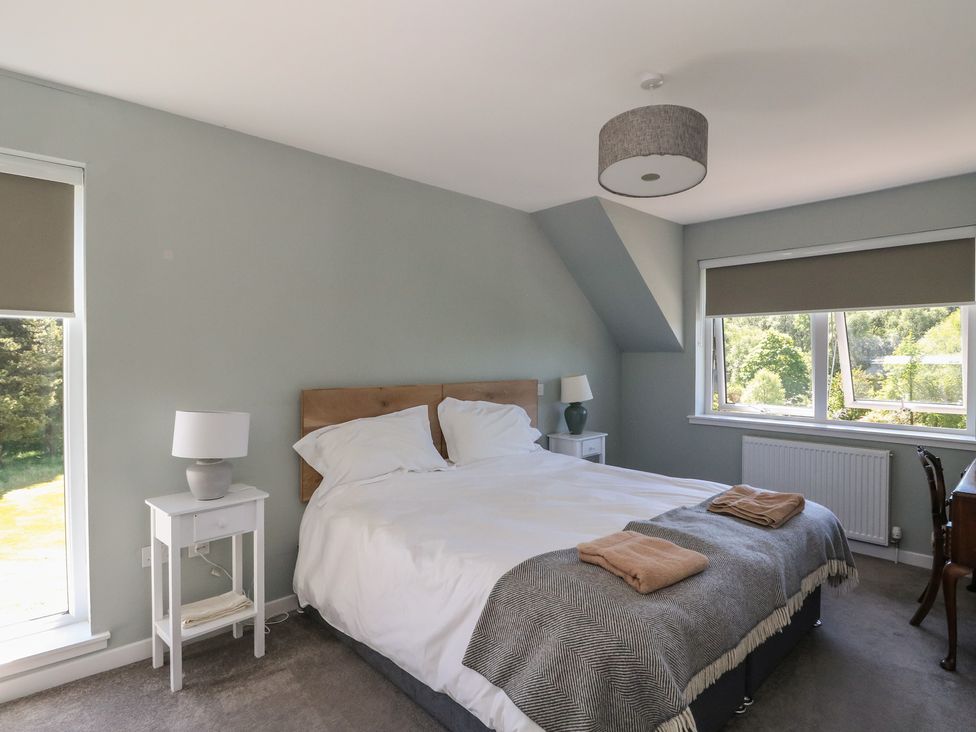 A bedroom with a double bed bedside tables with lamps and windows with blinds at Sobrachan in Kilmartin