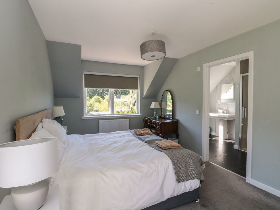 A bedroom with a bed a bedside lamp a dressing table with a mirror and an ensuite bathroom at Sobrachan in Kilmartin