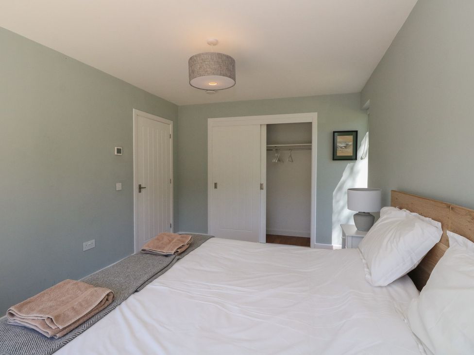 A bedroom with a bed with white bedding and folded towels on a blanket a bedside table with a lamp a closet with sliding doors and a closed door at Sobrachan in Kilmartin