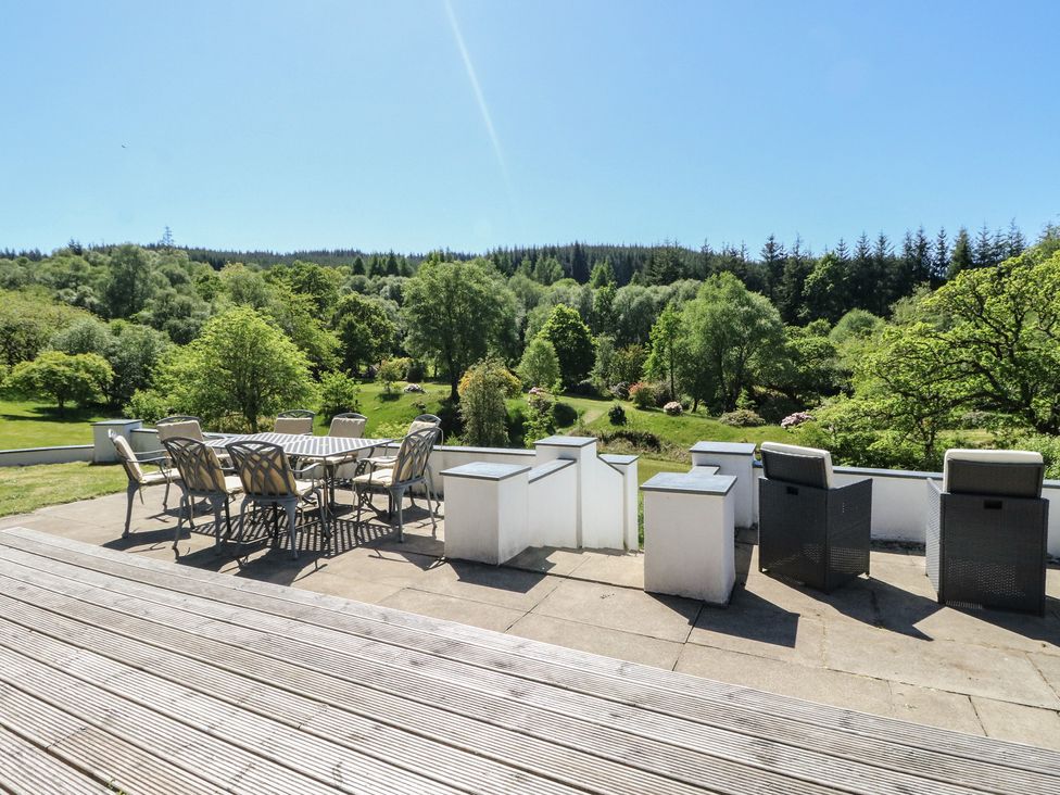 An outdoor patio with a table and chairs overlooking a green landscape with trees at Sobrachan in Kilmartin