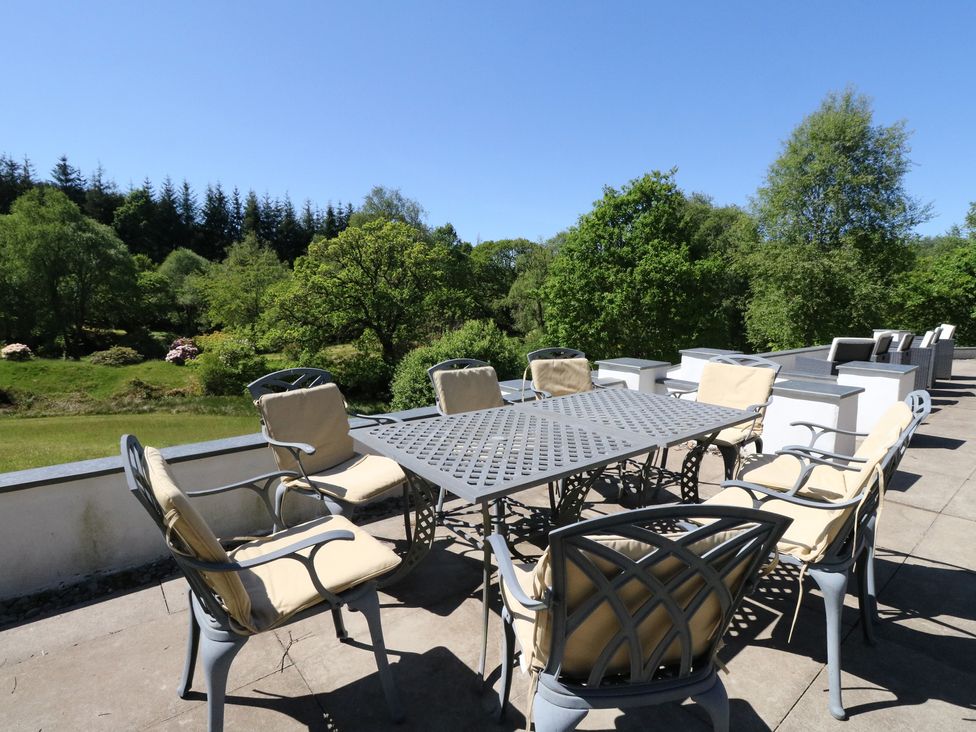 An outdoor patio with a metal table and cushioned chairs overlooking trees and greenery at Sobrachan in Kilmartin