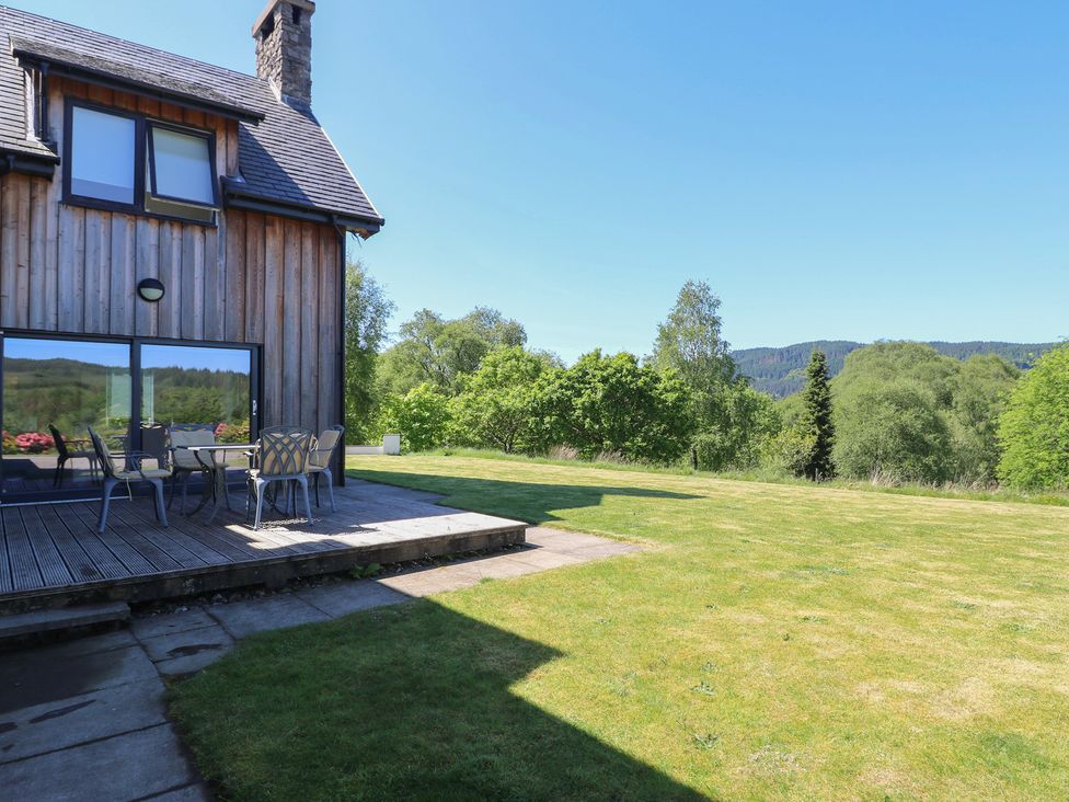 A wooden house with a patio table and chairs on a deck overlooking a grassy lawn and trees at Sobrachan in Kilmartin