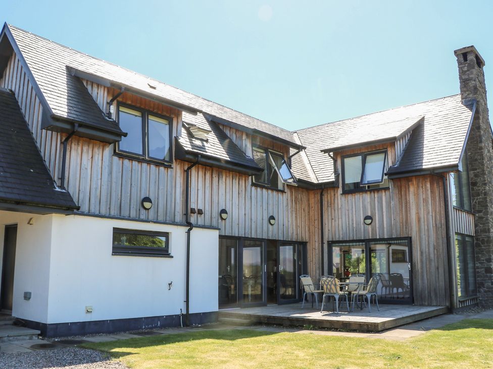A two-story house with wooden paneling and white walls with outdoor patio furniture on the wooden deck at Sobrachan in Kilmartin