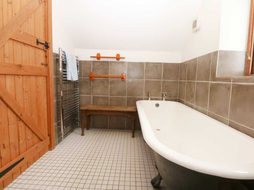 A bathroom featuring a bathtub and wooden bench at Beudy Mawr Y Felinheli