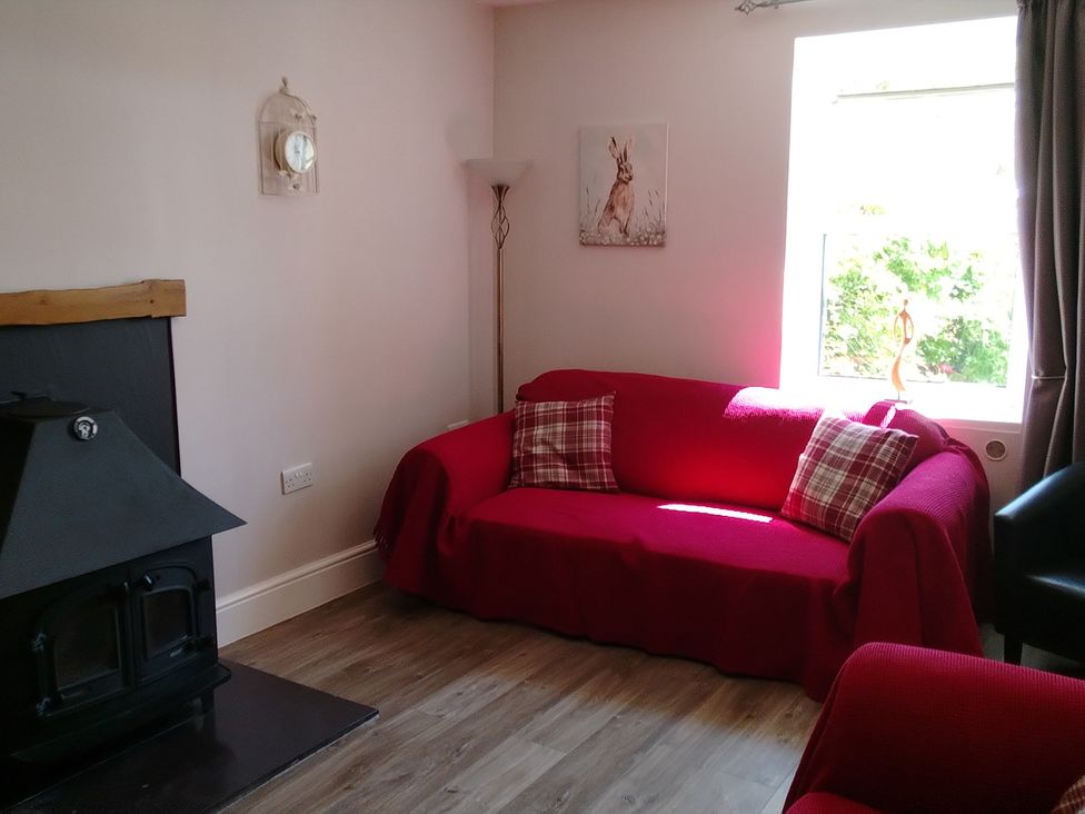 A living room with a red sofa and a clock at The Farmhouse in Brynsiencyn near Newborough