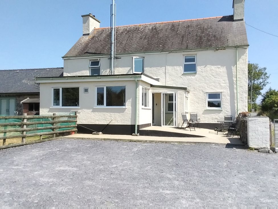 An exterior view of a house with a patio and chairs at The Farmhouse in Brynsiencyn near Newborough