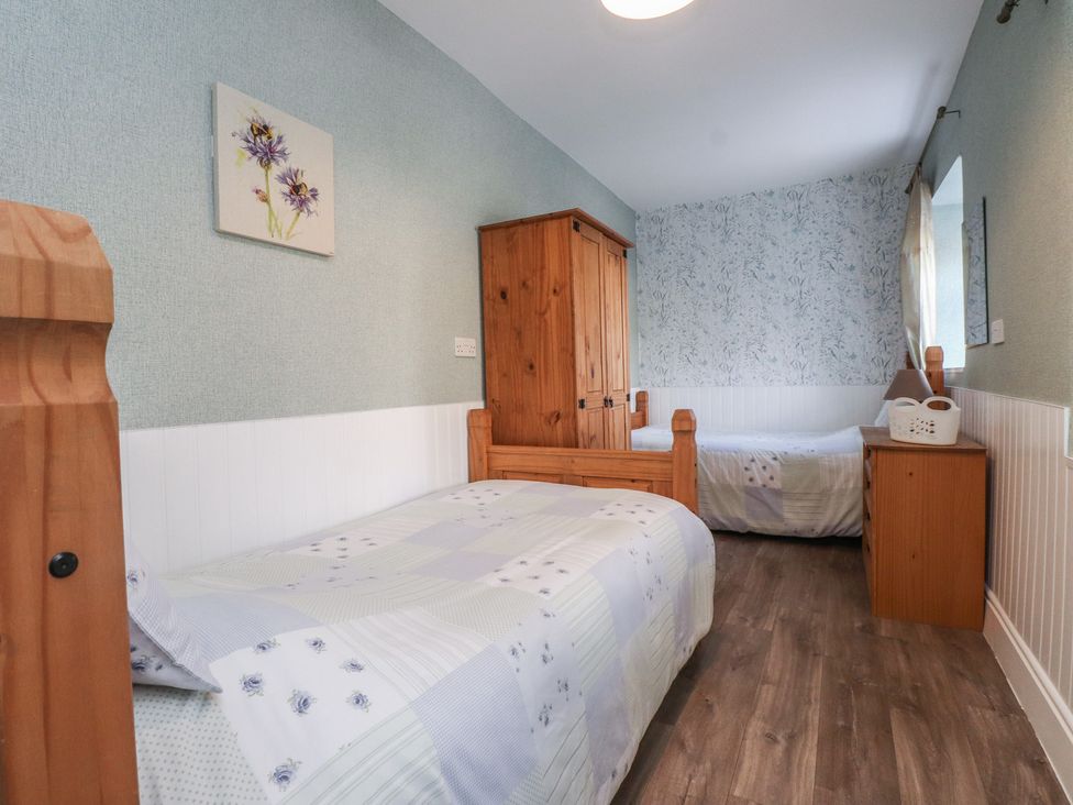 A bedroom with two beds and a wooden wardrobe at The Farmhouse in Brynsiencyn near Newborough