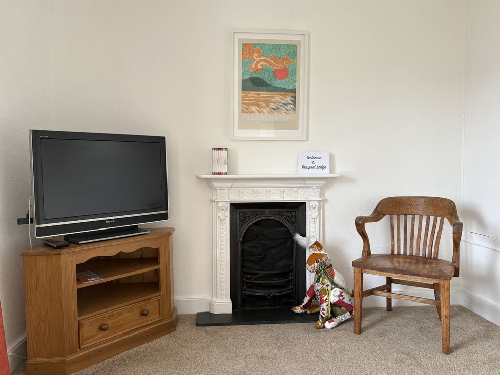 A living room with a television, chair, and fireplace at Prospect Lodge in Portinscale