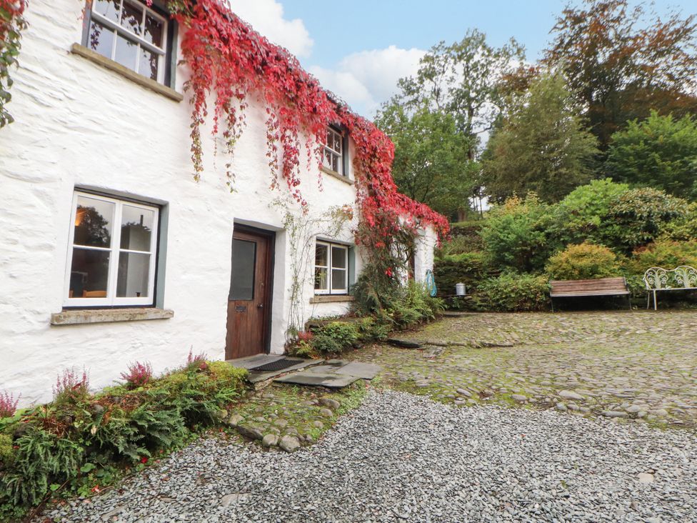 An outdoor view of a white house with plants and a gravel path at Mill Cottage in Garnett Bridge