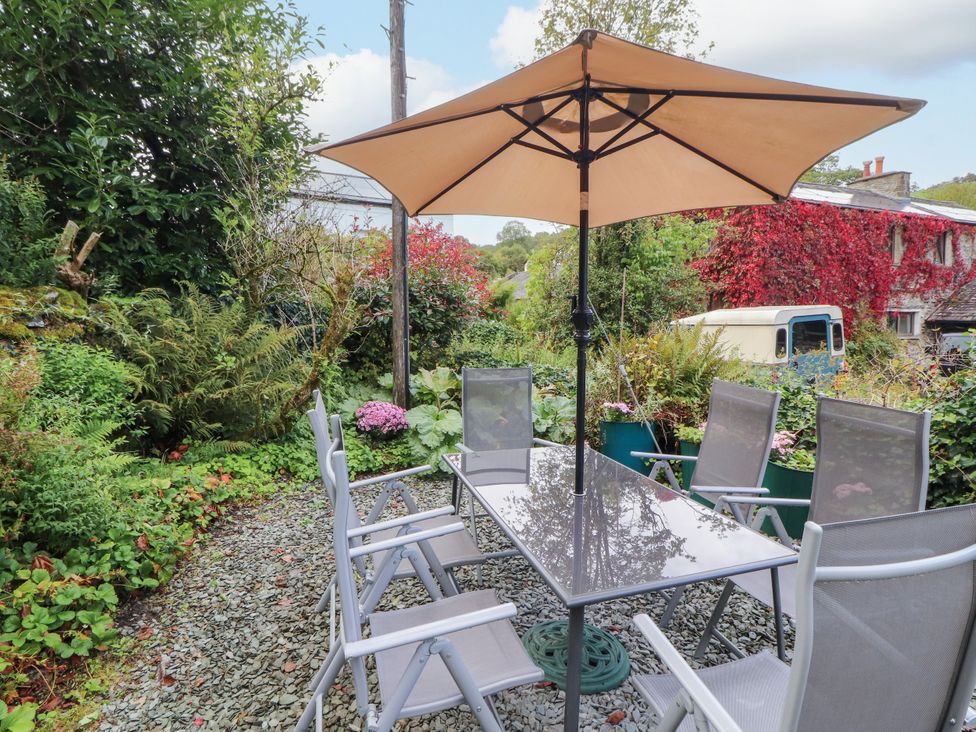 A garden with a table and chairs under an umbrella at Mill Cottage Garnett Bridge