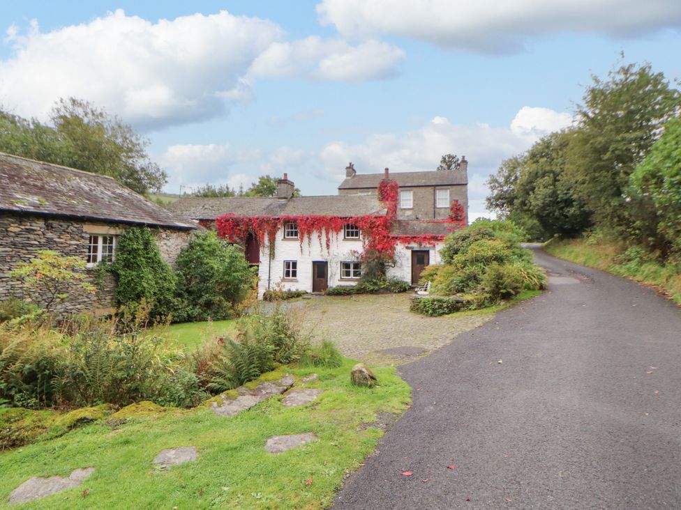 A cottage with ivy on the walls and a driveway at Mill Cottage in Garnett Bridge