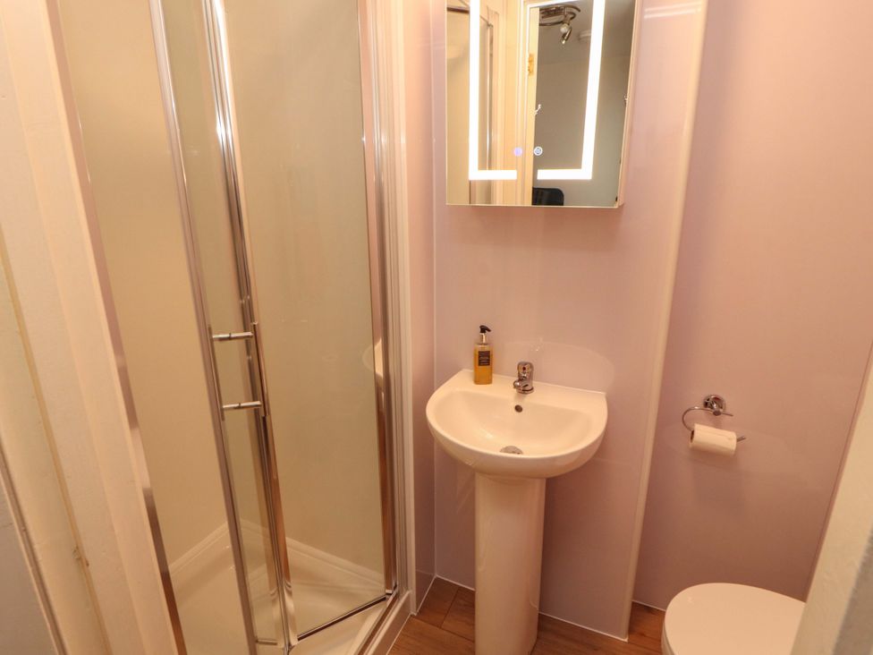 A bathroom with a shower, wash basin, mirror, and toilet at Archers in Keswick