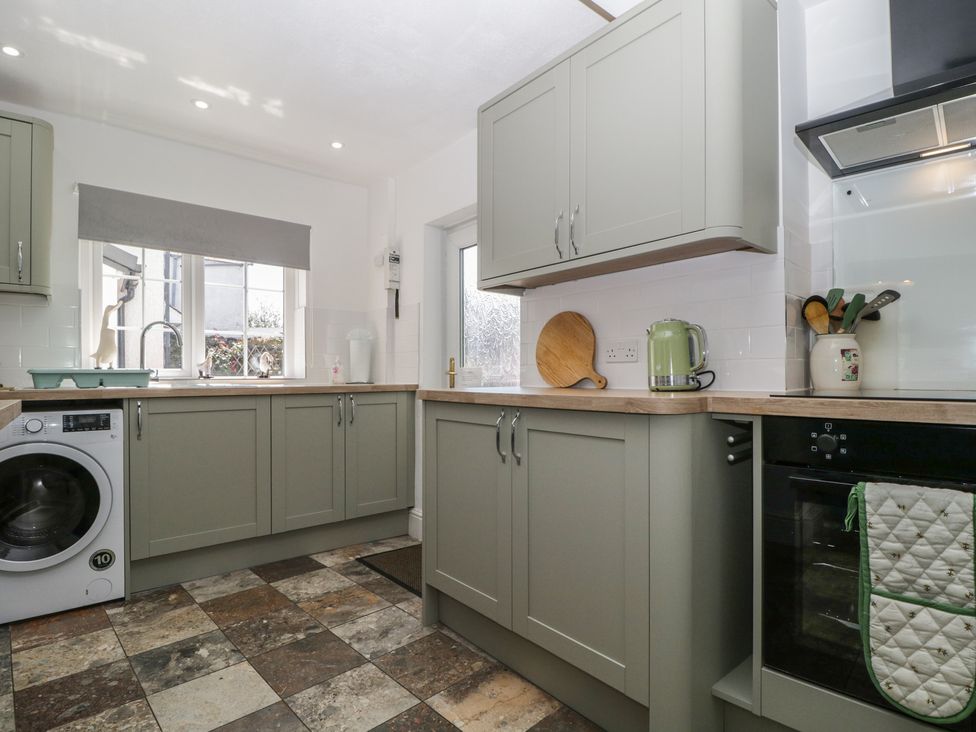 A kitchen with cabinets, sink, washing machine, and appliances at Fountain Cottage in Keswick