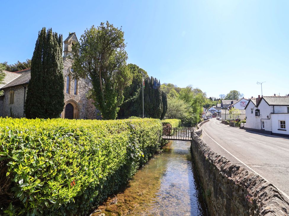 A church with a hedge and a stream next to a road at Ty Cerrig in Dyserth