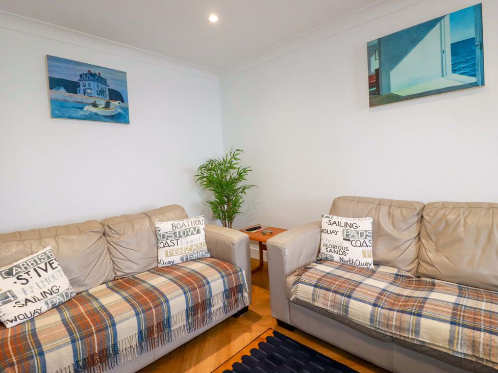 A living room with two beige sofas covered with plaid throws and cushions a wooden side table with a plant between the sofas and paintings on white walls at Pink House in Mevagissey