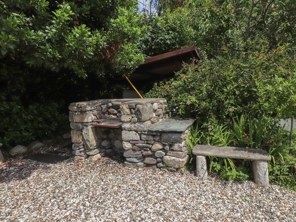 An outdoor area with a stone barbecue and a bench at Plas Mawr in Groeslon