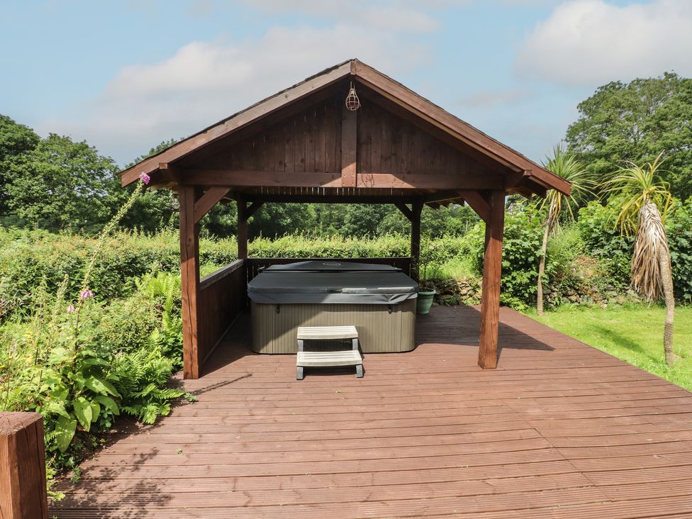A wooden gazebo with a hot tub on a deck at Beudy'r Wennol in Groeslon