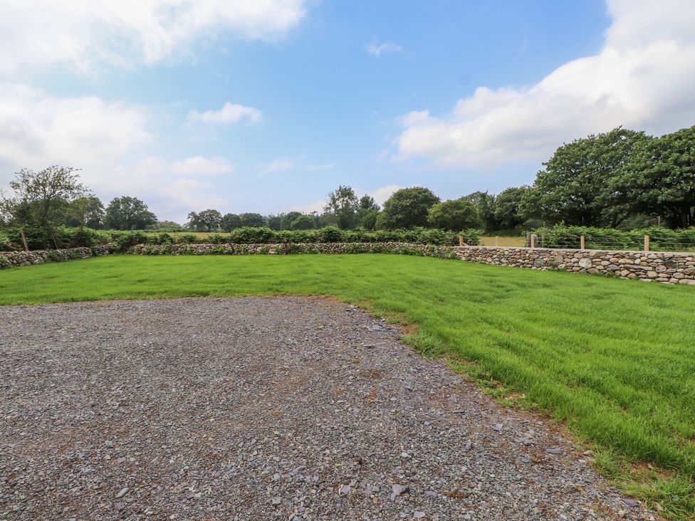 A garden with a stone wall and grass area at Beudy'r Wennol Groeslon
