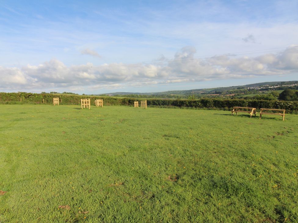 An outdoor area with wooden benches and grass at Cherry Lodge in Lanivet near Bodmin