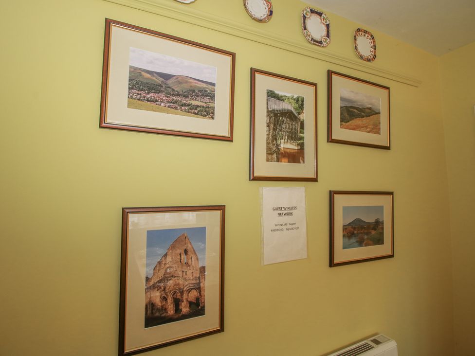 A wall with framed pictures and wireless network information at Wash House Cottage Much Wenlock